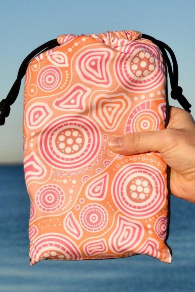 Walkabout Indigenous Beach Towel folded in eco-friendly travel bag, showcasing the vibrant orange Aboriginal design with walkabout symbols and traditional patterns that connect travelers to the sacred journey and spiritual relationship with country